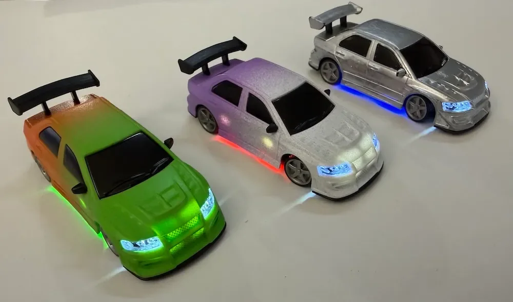 Trois carrosseries RC 1/76 côte à côte, phares et bandeaux LED allumés sous le châssis