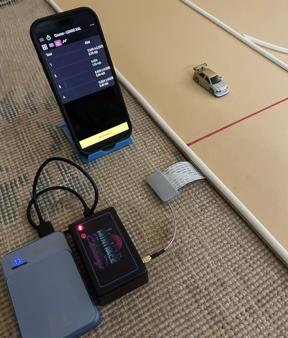 Système Mini Race Challenge installé près d’une piste RC 1/76, avec smartphone, boîtier et antenne sous le tapis