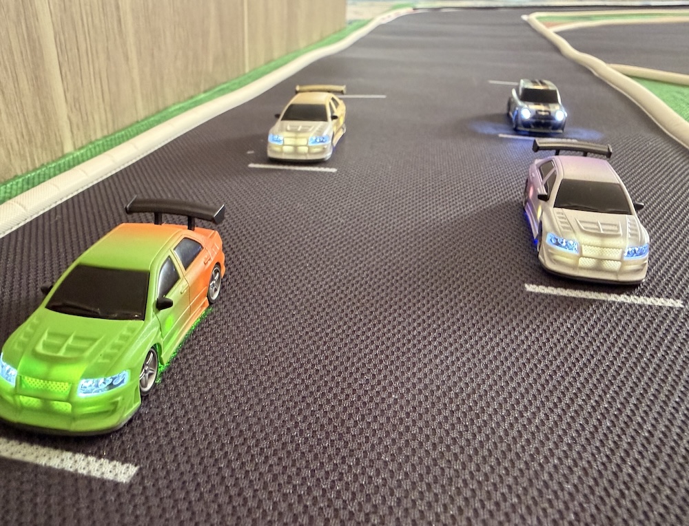 Quatre voitures RC 1/76 éclairées et alignées sur la grille de départ d’un tapis de course